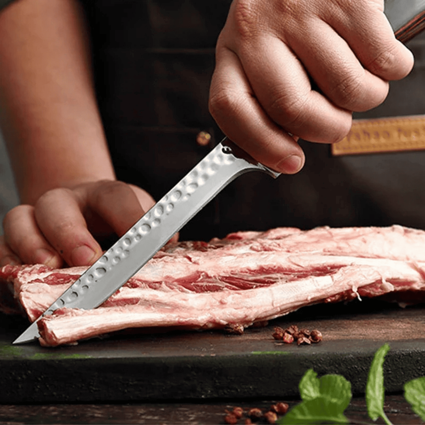 Person cutting raw meat with a knife on a wooden surface