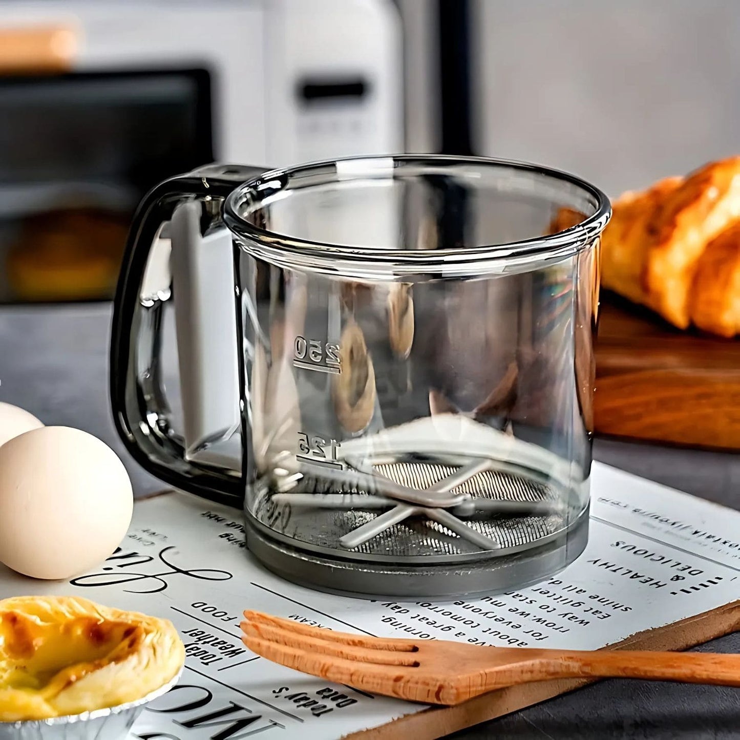 One-handed flour sifter in use, dusting powdered sugar over croissants