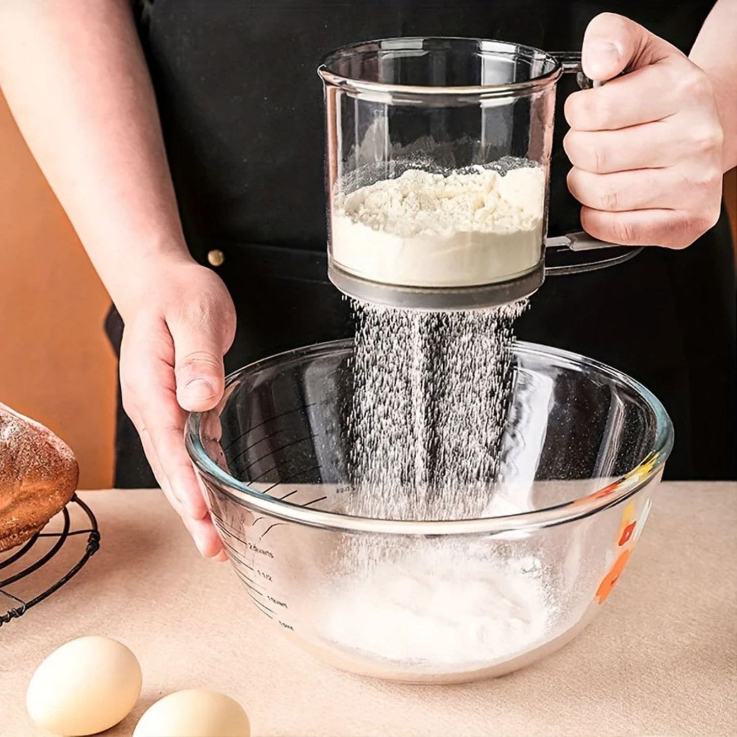 One-handed flour sifter in use, dusting powdered sugar over croissants