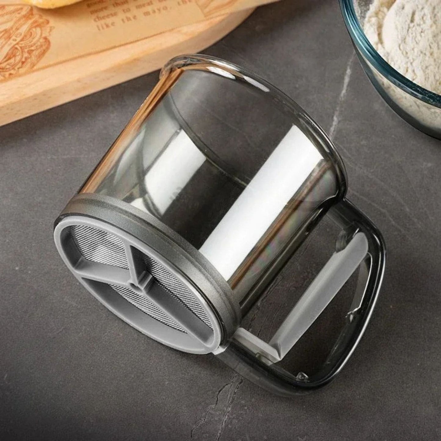 One-handed flour sifter in use, dusting powdered sugar over croissants