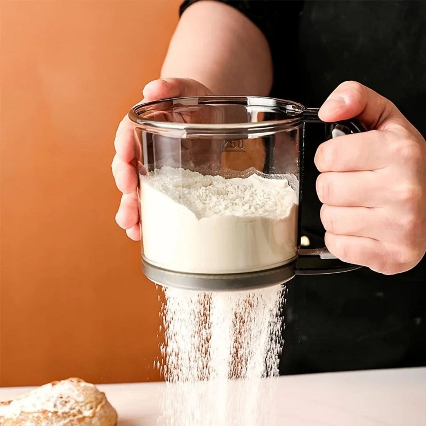 One-handed flour sifter in use, dusting powdered sugar over croissants
