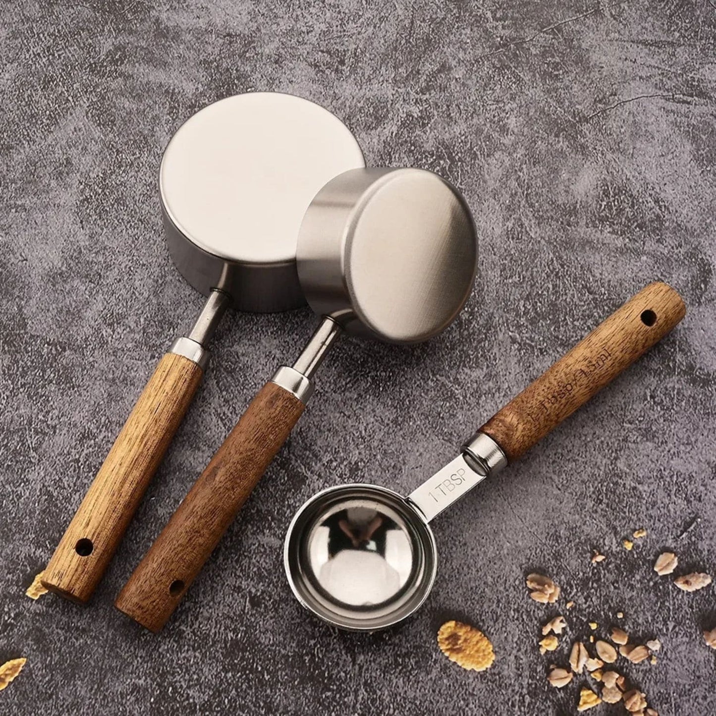 Silver measuring spoons and cups with wooden grips, displayed with flour and sugar