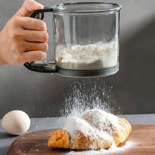 One-handed flour sifter in use, dusting powdered sugar over croissants