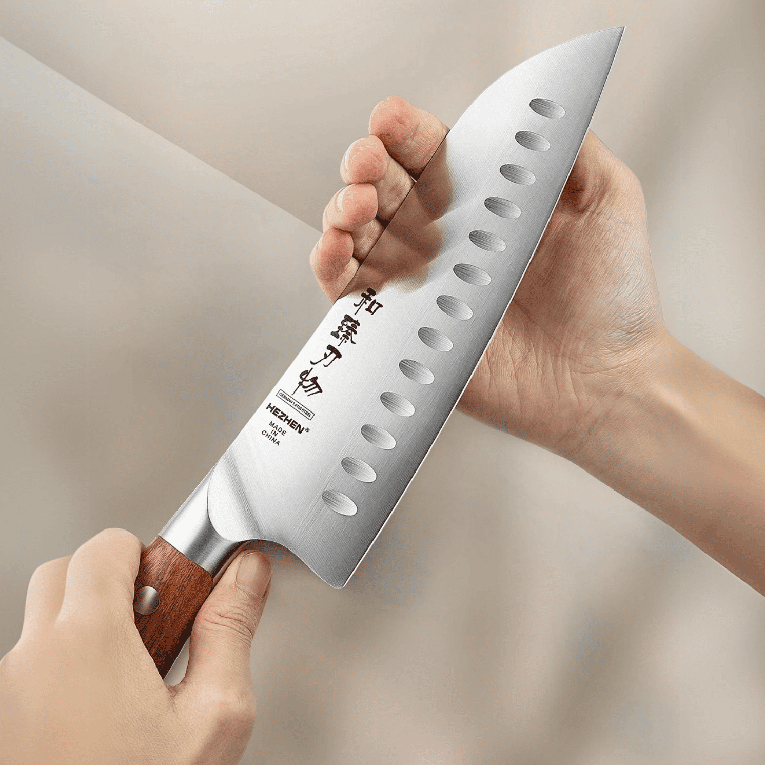 Hand holding a chef's knife with a brand logo on a neutral background